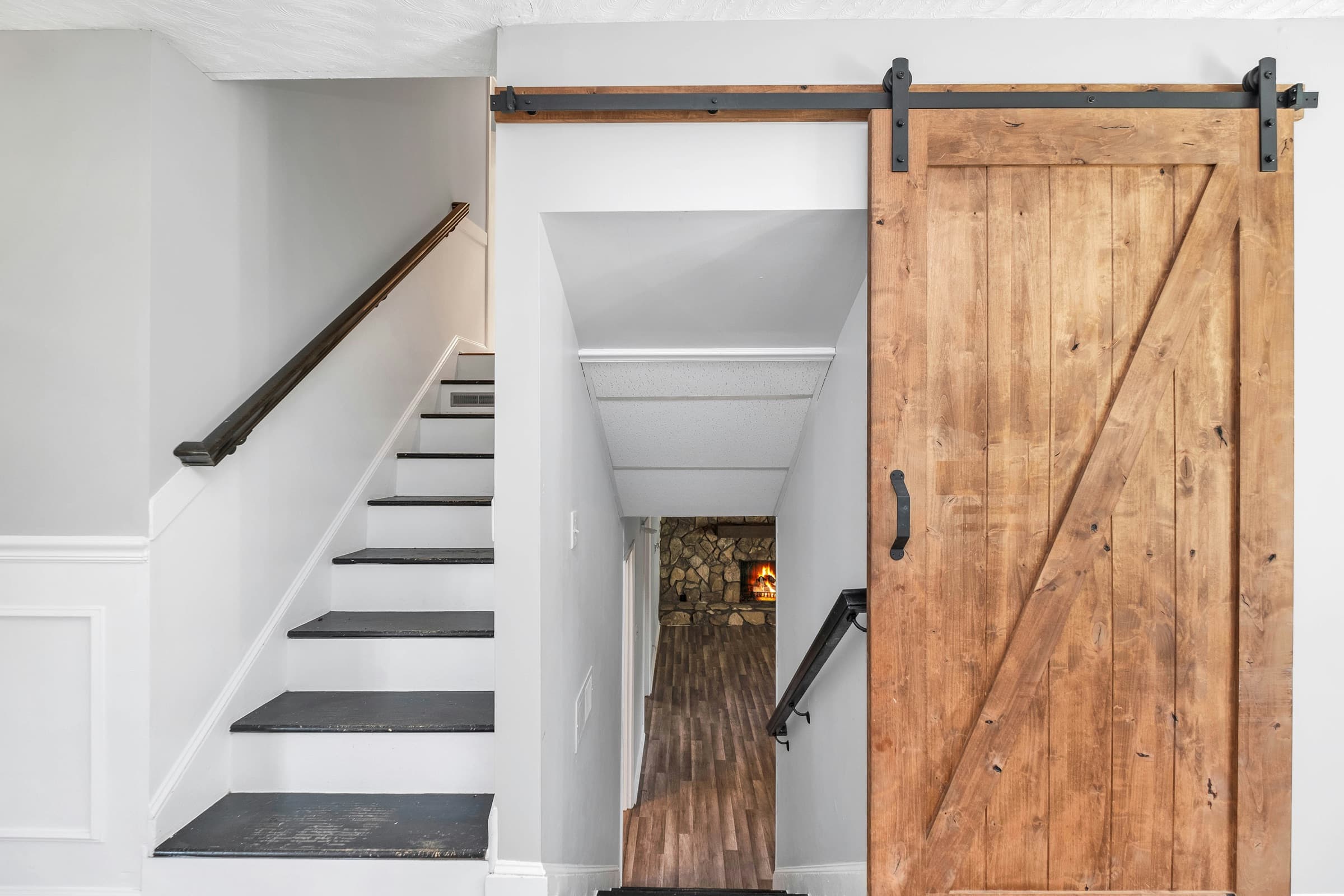 Natural wood barn door installed on black sliding hardware beside a stairway
