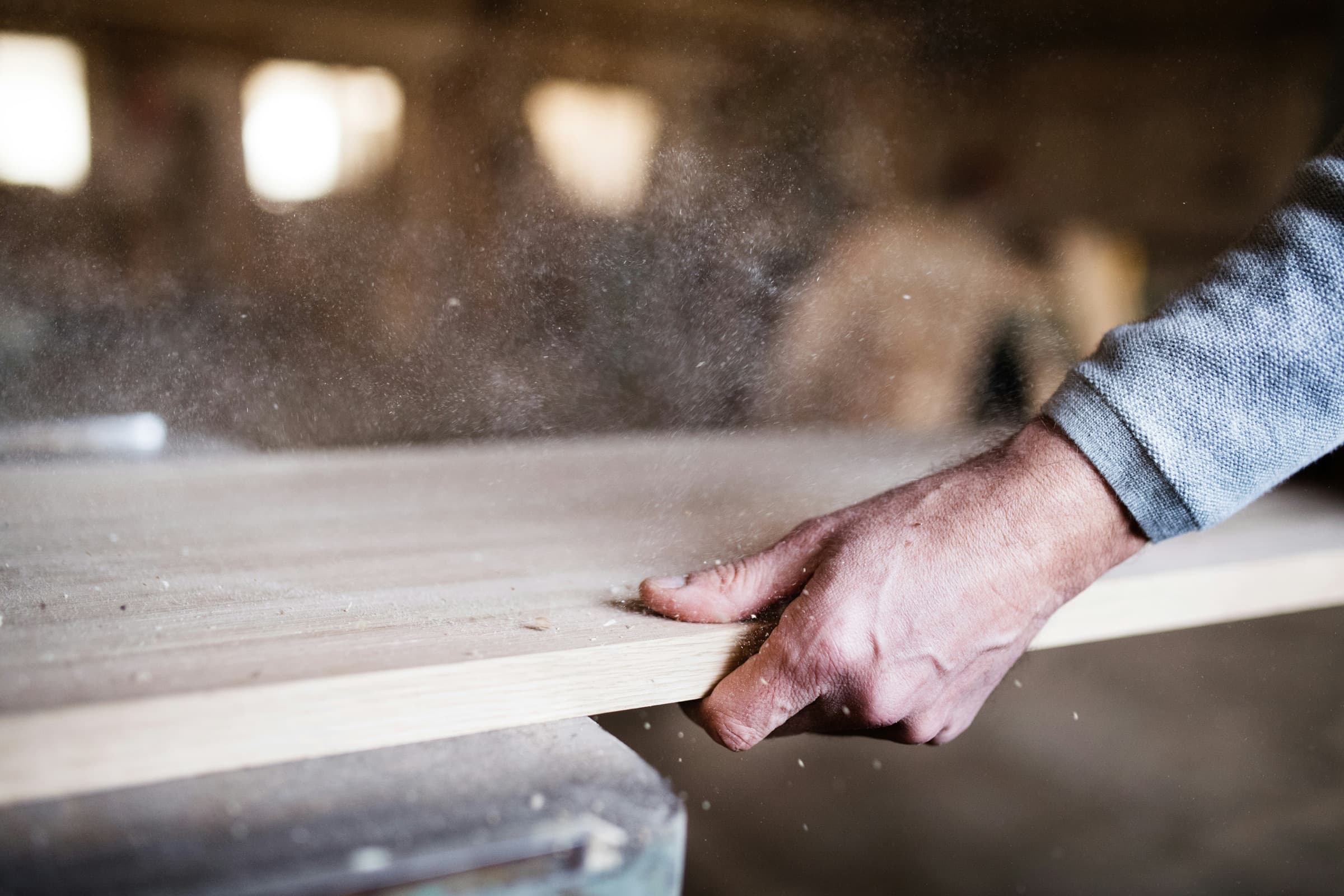 Carpenter guiding a wood board through a saw as sawdust rises