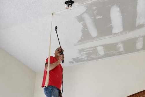 Handyman repairing a drywall ceiling from a scaffold