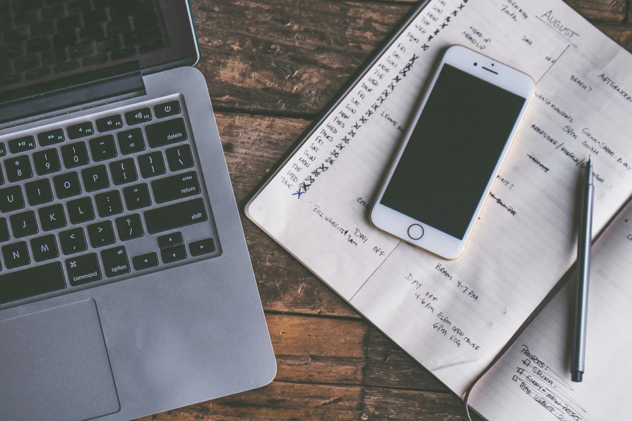 Handwritten task list beside a phone and laptop on a wood table