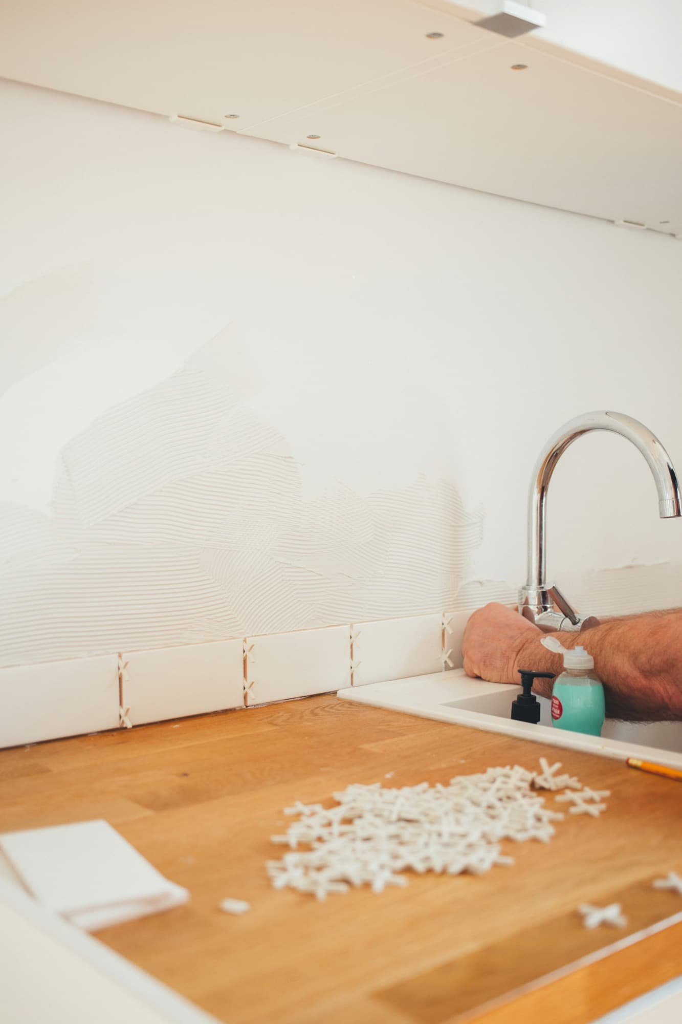 White tile backsplash being installed behind a kitchen sink