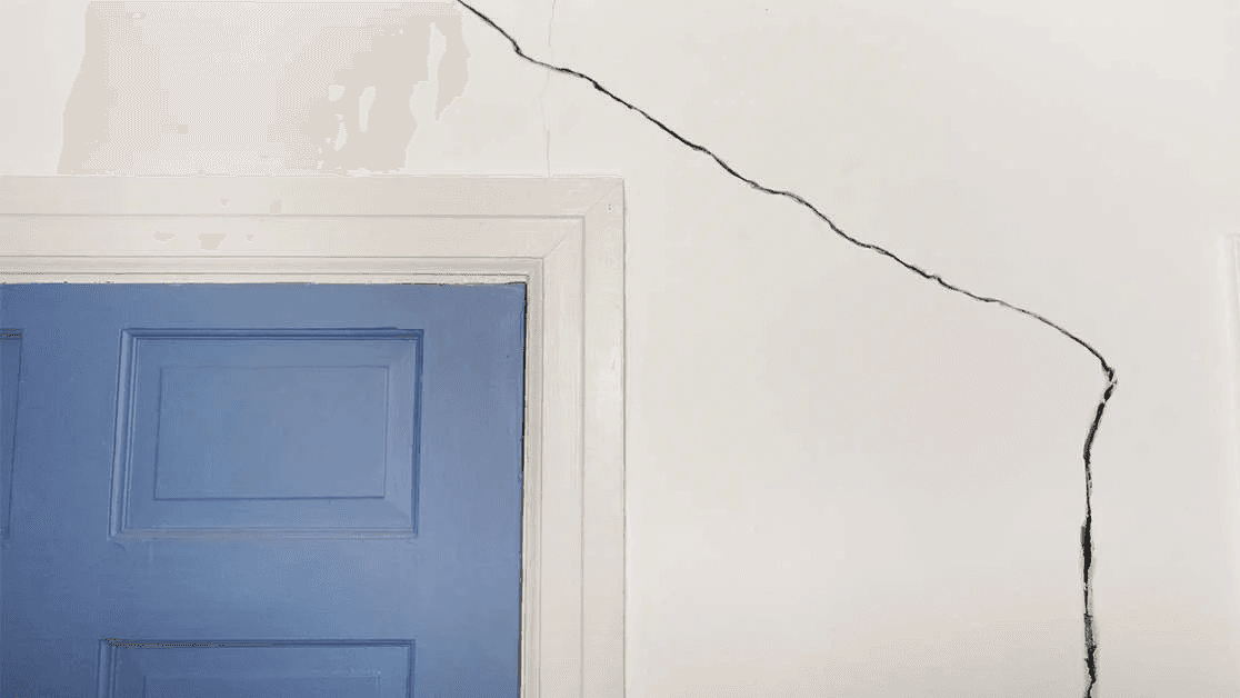 Large diagonal drywall crack above a blue interior door