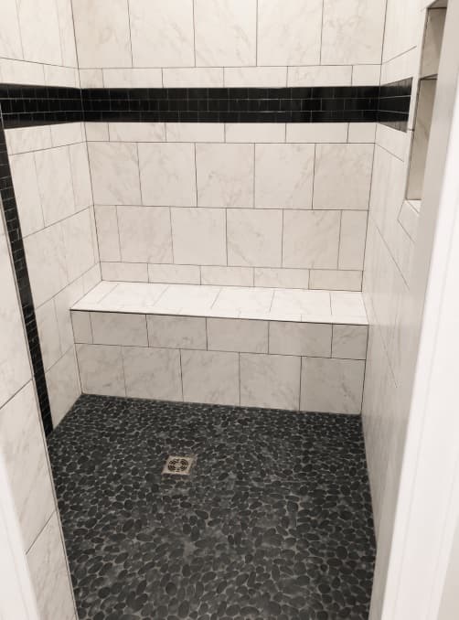 White tiled shower with long bench and black pebble floor