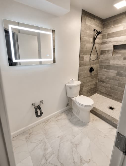 Compact finished bathroom with illuminated mirror and tiled shower