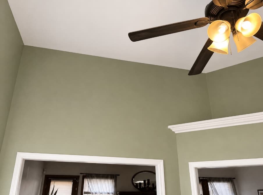 Finished vaulted room with sage walls, white trim, and ceiling fan
