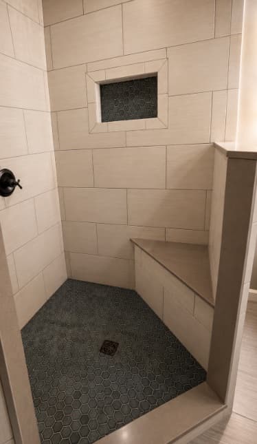 Gray tile shower with a built-in bench and mosaic floor