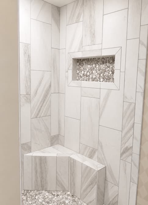 Finished white tile shower with a built-in bench and mosaic niche